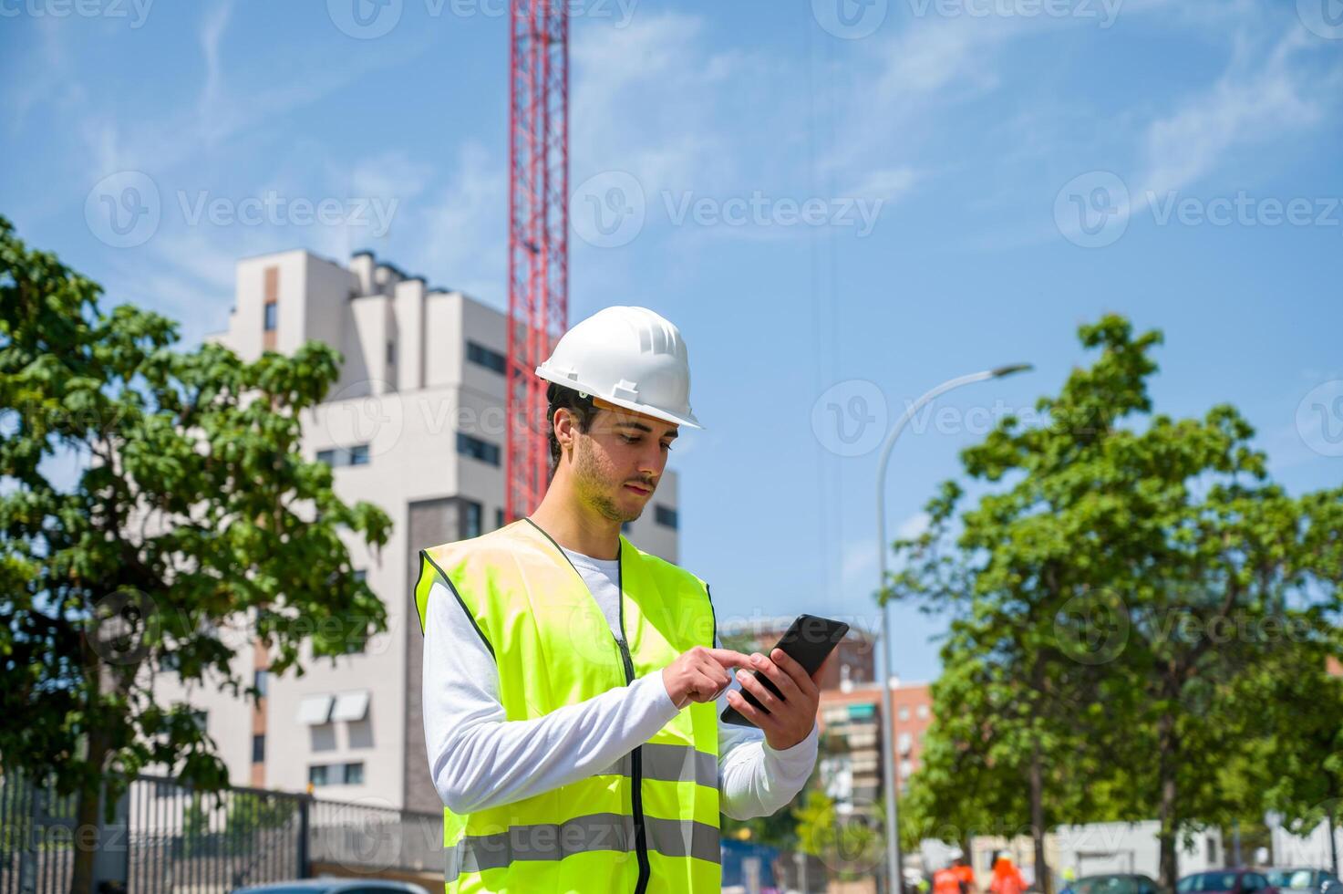 Professional young male construction worker with safety helmet and reflective vest at a construction site with building progress in the background3 photo