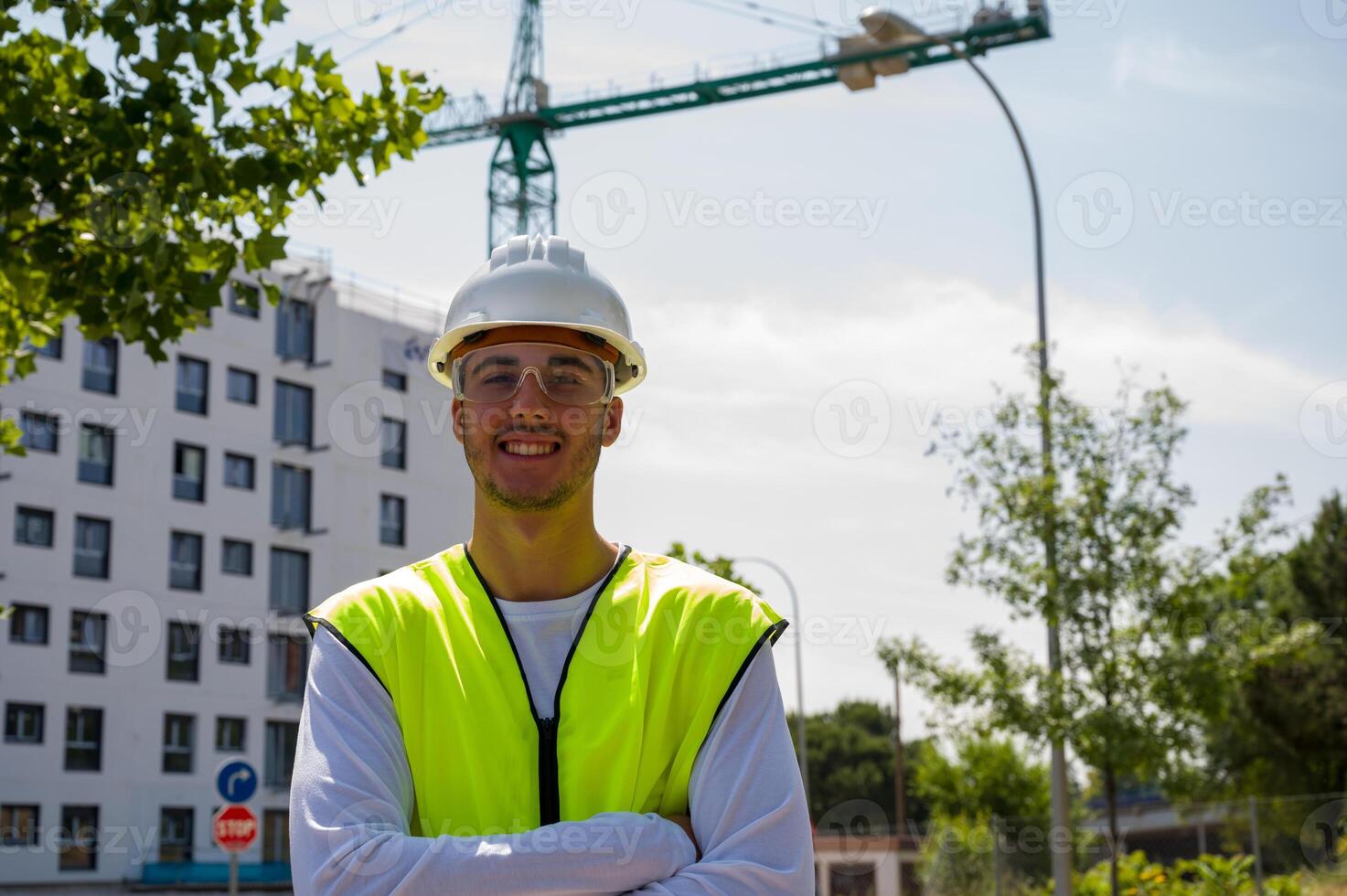 Professional male construction worker with safety helmet and reflective vest smiling confidently at a construction site with building progress in the background photo