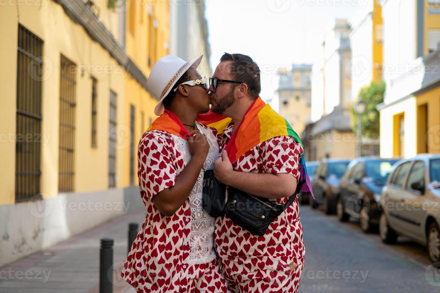 Portrait of a multi-ethnic gay couple raising lgbt flag in the street in love, photo
