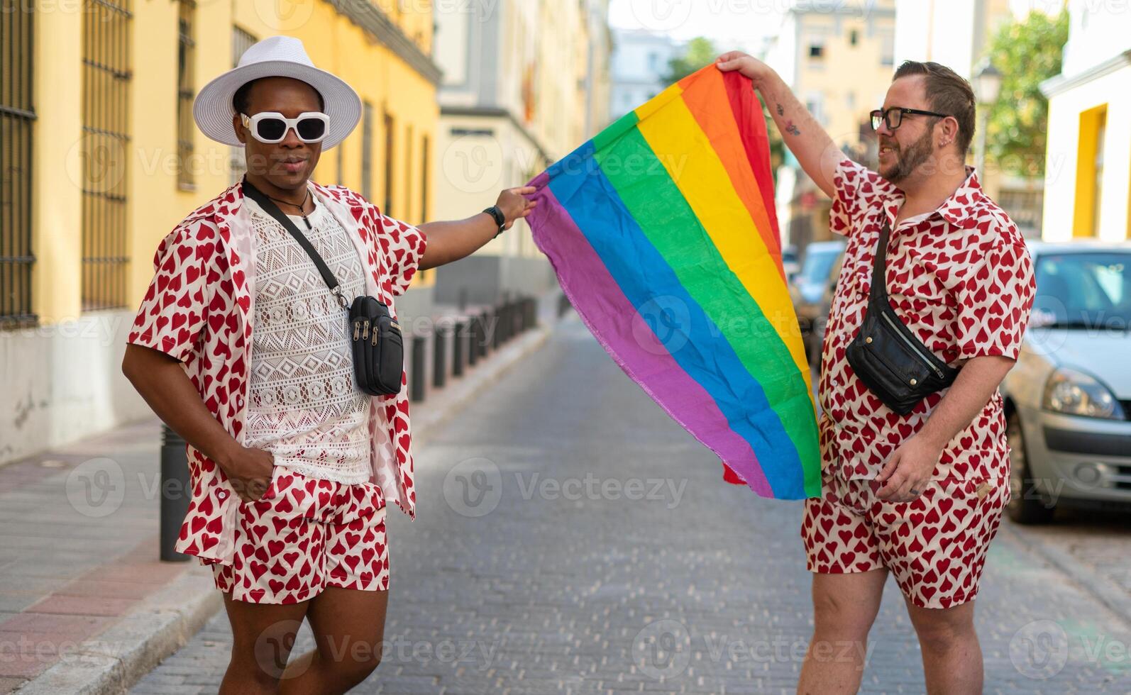 Portrait of a multi-ethnic gay couple raising lgbt flag in the street.... photo