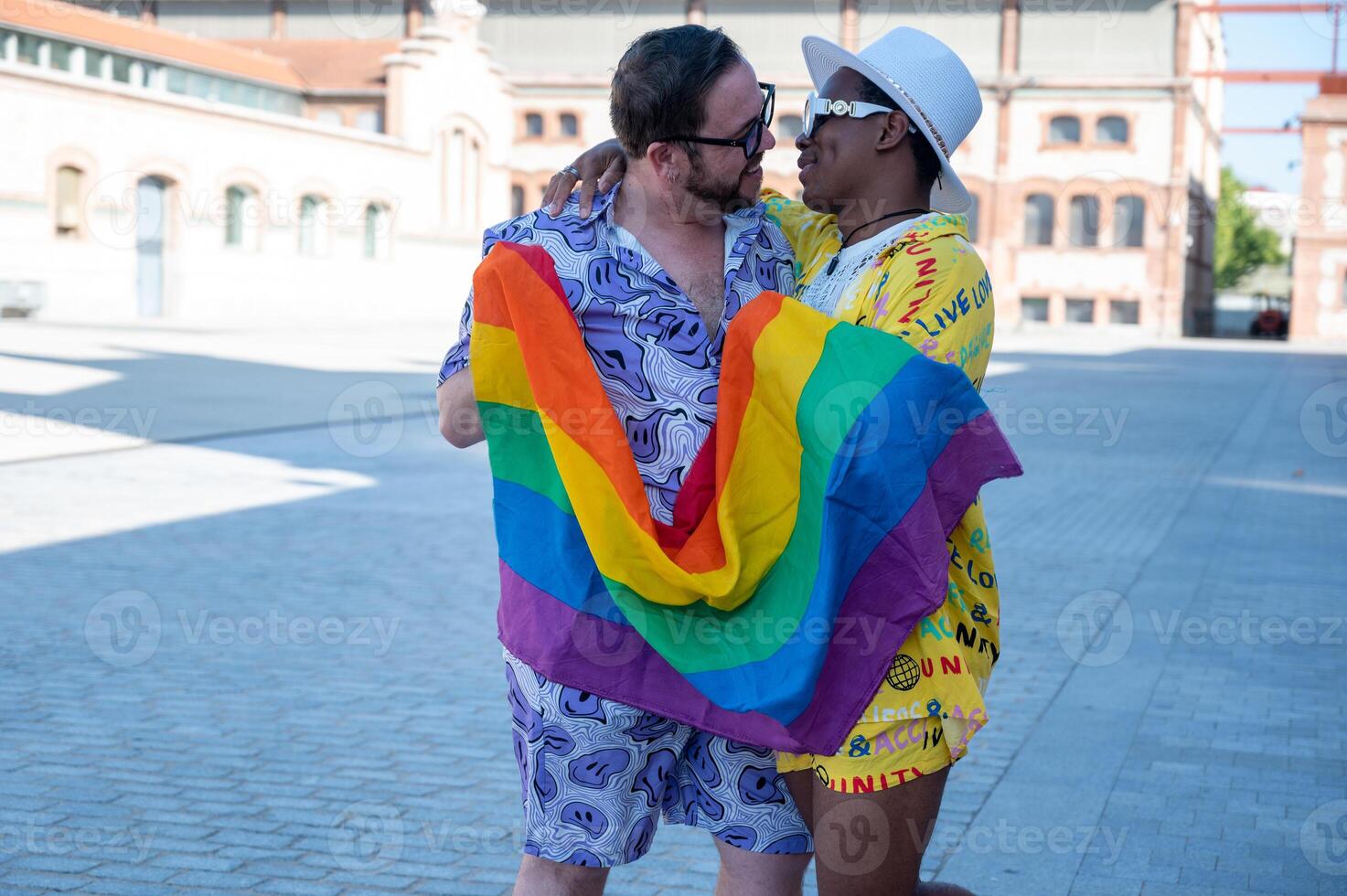 Portrait of a multi-ethnic gay couple raising lgbt flag in the street. photo