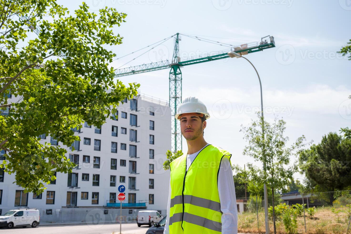 Professional young male construction worker with safety helmet and reflective vest at a construction site with building progress in the background.. photo