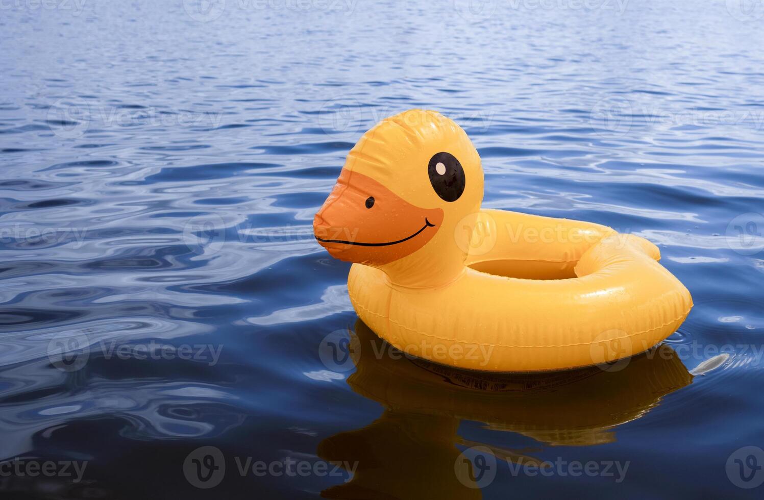 Bright yellow duck float resting on calm water surface at a lake photo