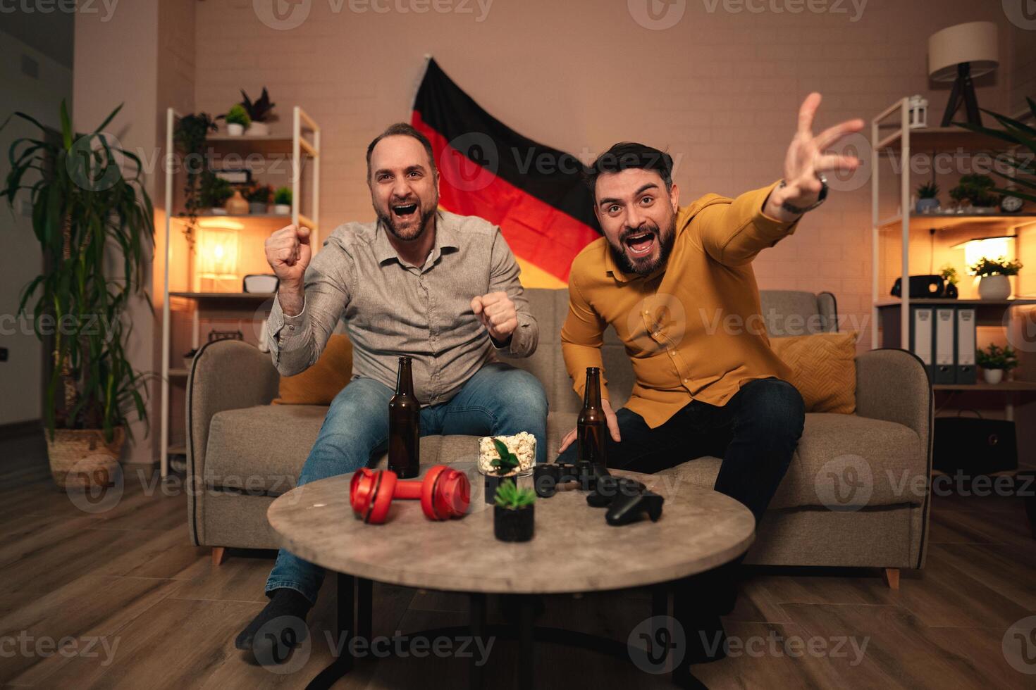 Friends celebrating a victory while watching sports in a cozy living room with a German flag photo