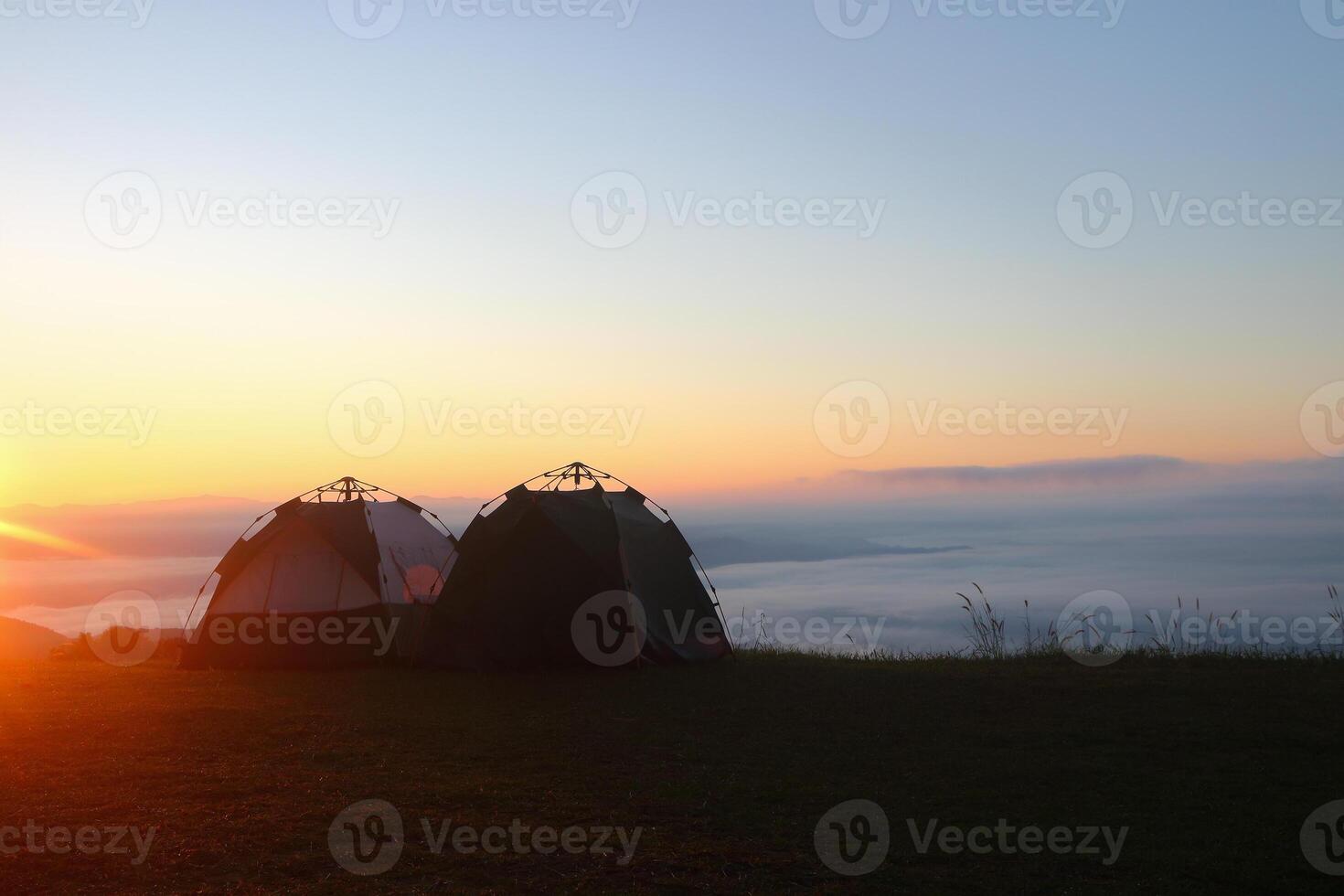 two tents for camping on top of mountain with sea of mist and sunshine in the morning. photo