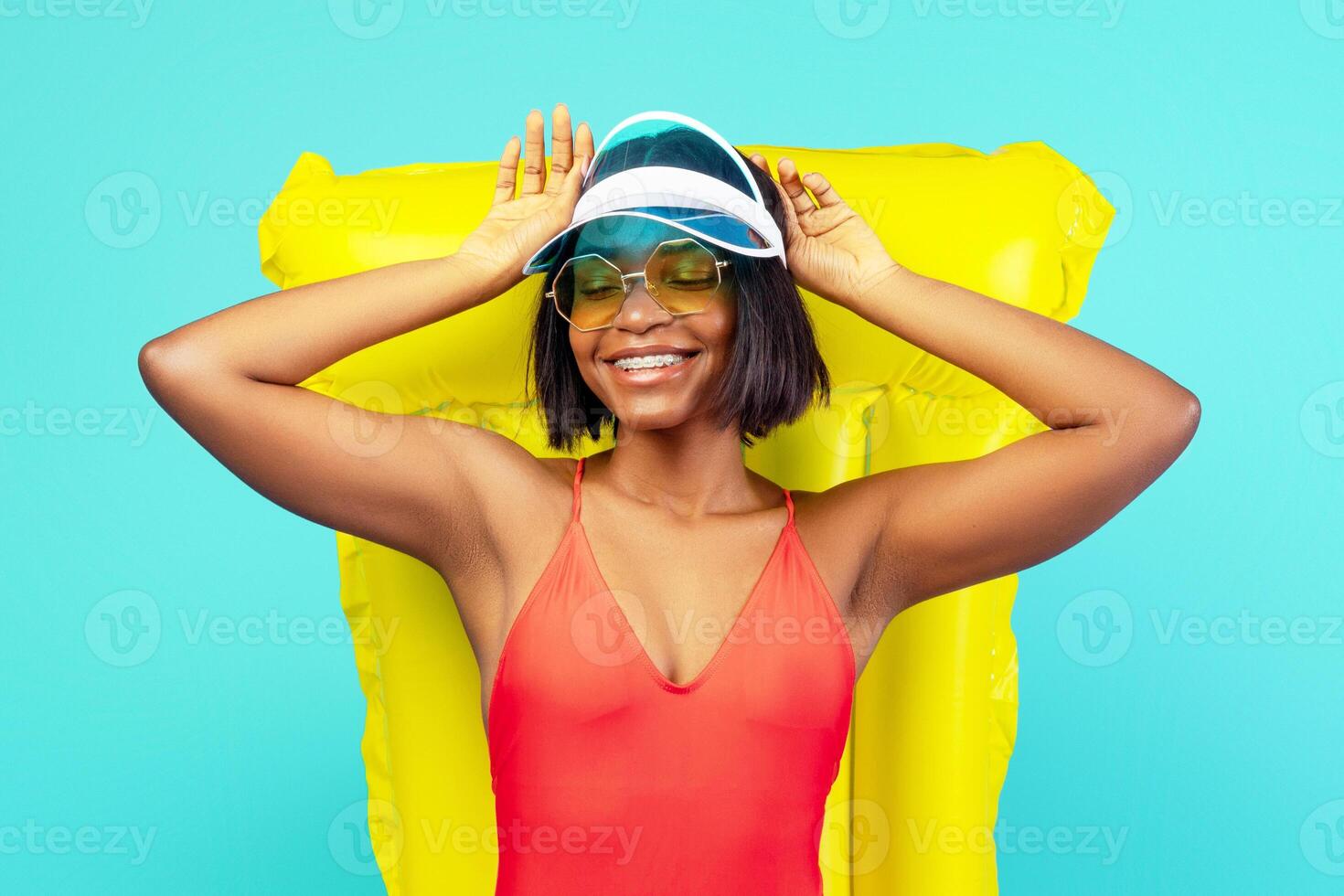 Summer vacation. Beautiful black woman in swimsuit lying on inflatable lilo, sunbathing on beach, blue studio background. Charming young lady relaxing and enjoying lazy day on pool float photo