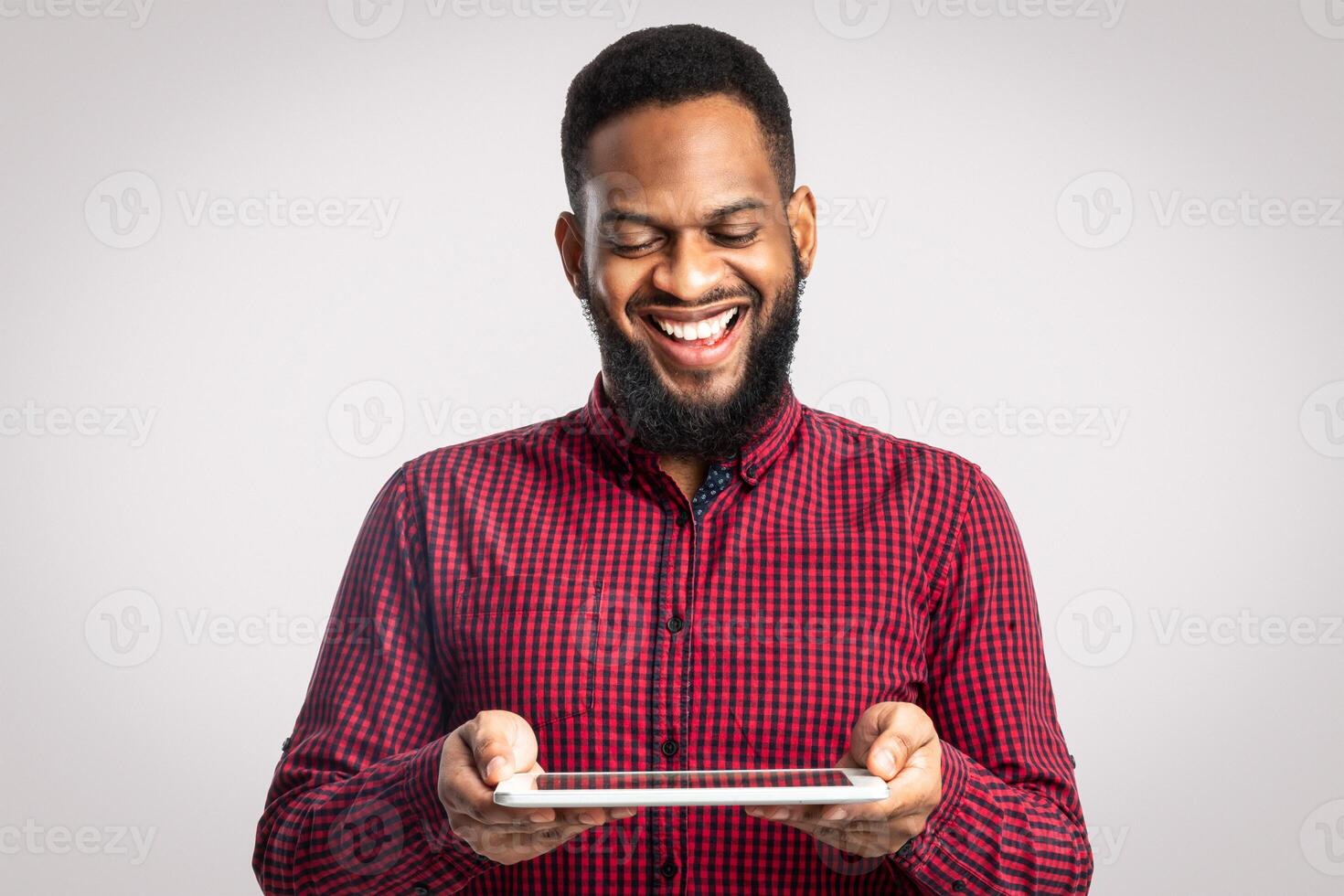 Cheerful African American Man Holding Digital Tablet Standing On White Background. Bearded Black Guy Playing Computer Game Online In Studio. Website, Internet Service And New Application Advert photo