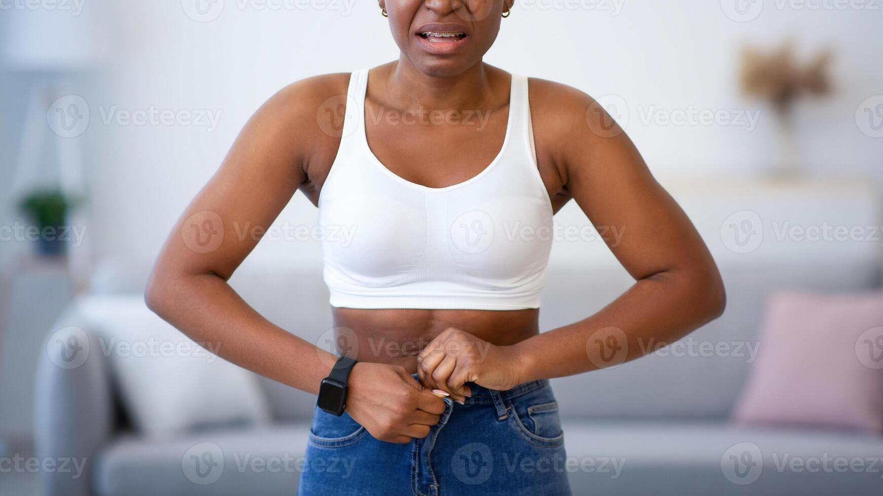 Frustrated Black Woman Buttoning Small Jeans After Weight Gain Standing At Home, Looking At Camera. Slimming Issue, Visceral Fat And Cellulitis, Weight-Loss Problem Concept photo