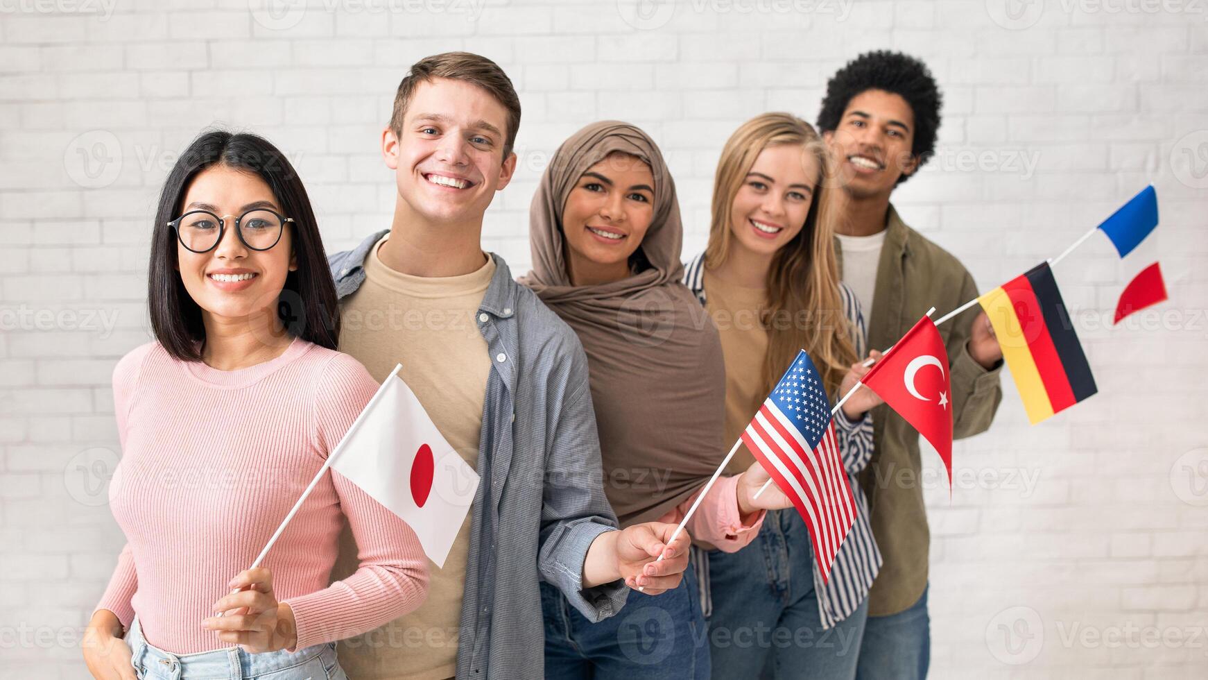 Exchange students and language school for different people. Funny digital young international pupils holding flags of USA, Japan, Turkey, Germany and France in classroom, studio shot, empty space photo