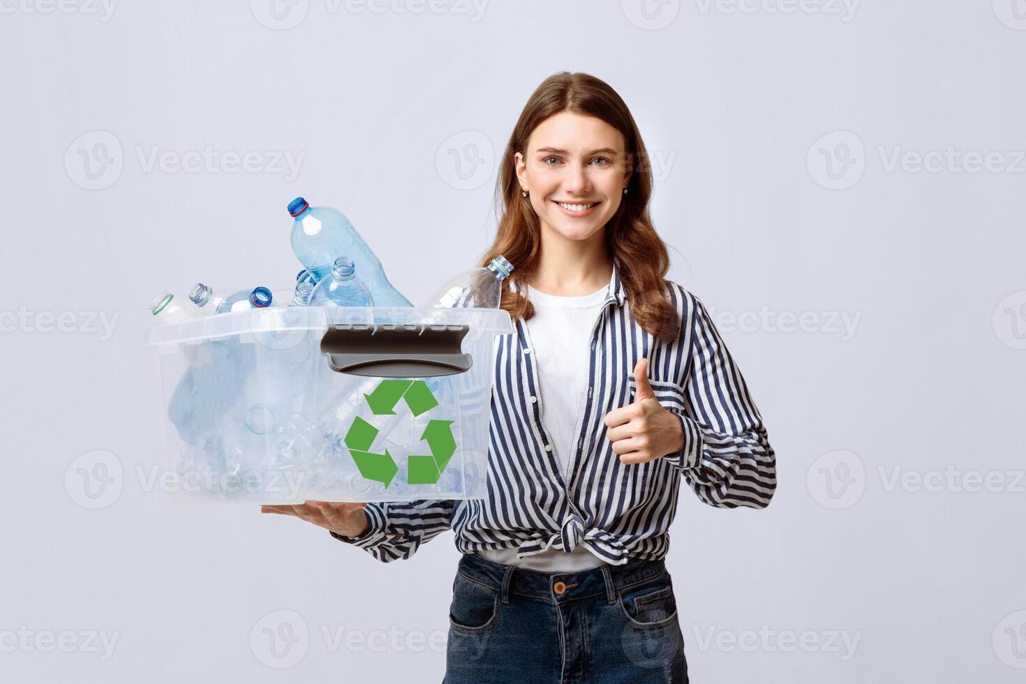 A young woman smiles while holding a recycling box filled with plastic bottles. She promotes eco-friendly practices and showcases her commitment to sustainability in an indoor setting. photo