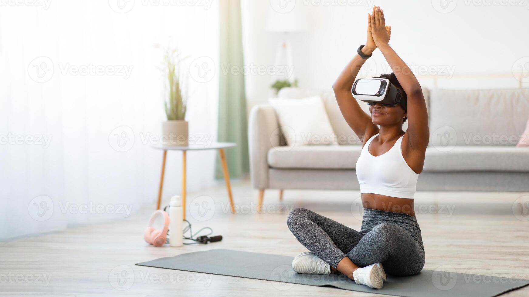 Black Woman Doing Yoga Wearing Virtual Reality Headset Training Sitting On Floor At Home. Smart Fitness, Digital Workout Via Augmented Reality Application Concept. Free Space For Text photo