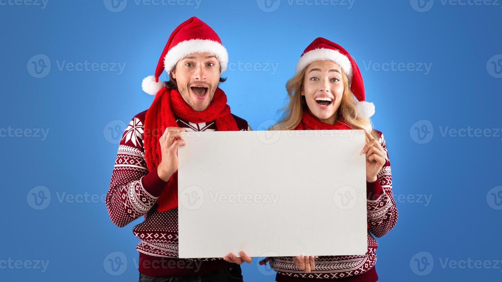 Christmas ad. Excited millennial couple holding empty poster with mockup for design over blue background photo