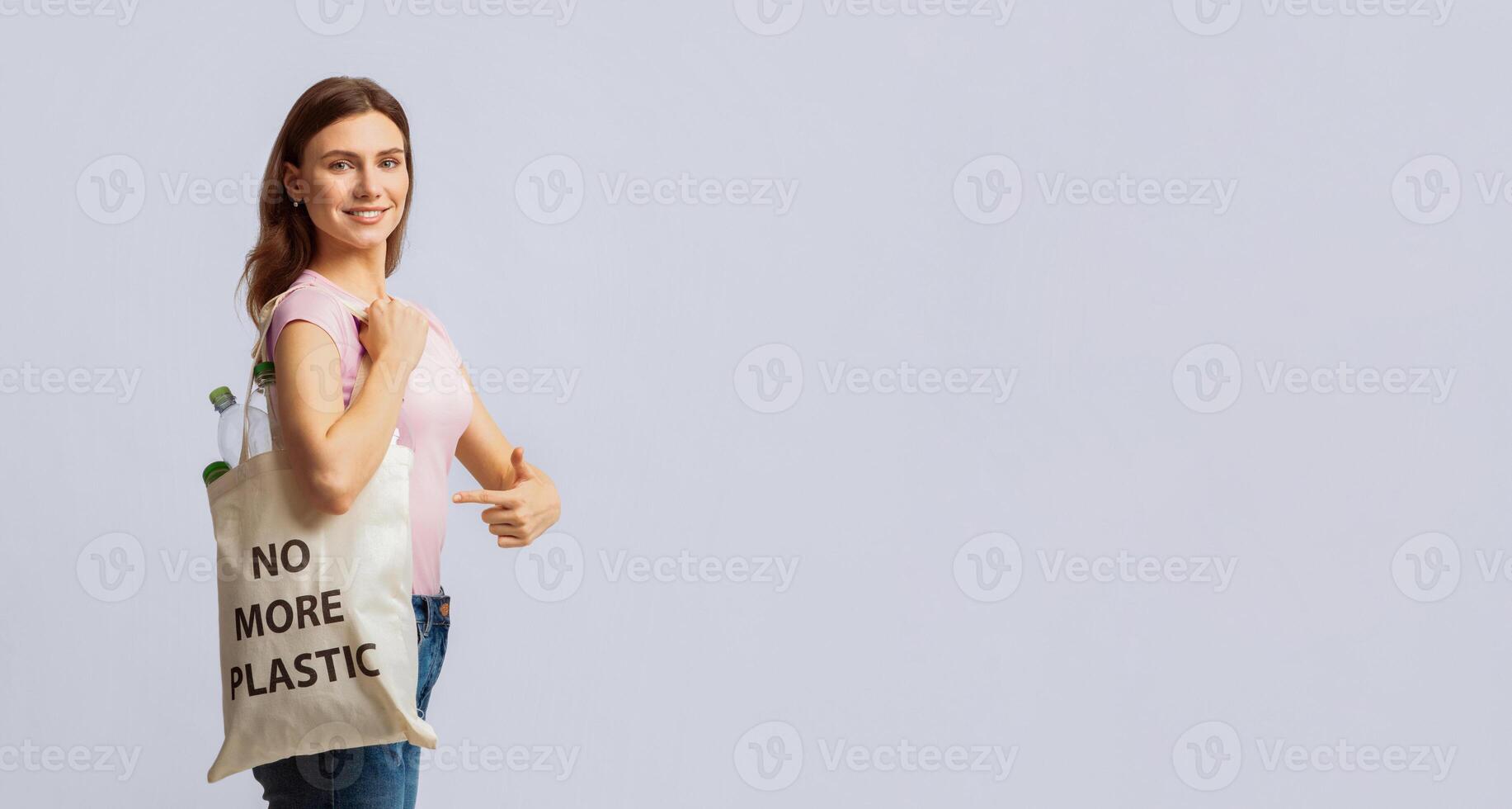 A woman stands confidently, holding a tote bag that says No More Plastic. She promotes recycling and eco-friendly practices, reflecting her commitment to sustainability, copy space photo