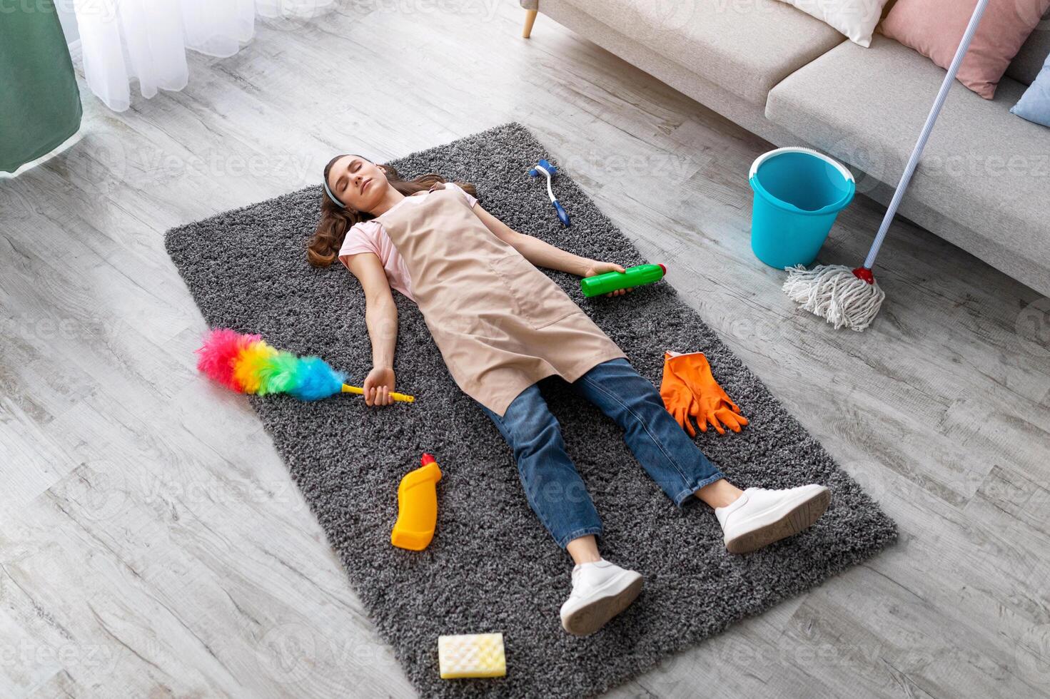 Above view of millennial woman sleeping on floor in living room, surrounded by cleaning supplies, exhausted from housework, tired from domestic chores, full length portrait photo