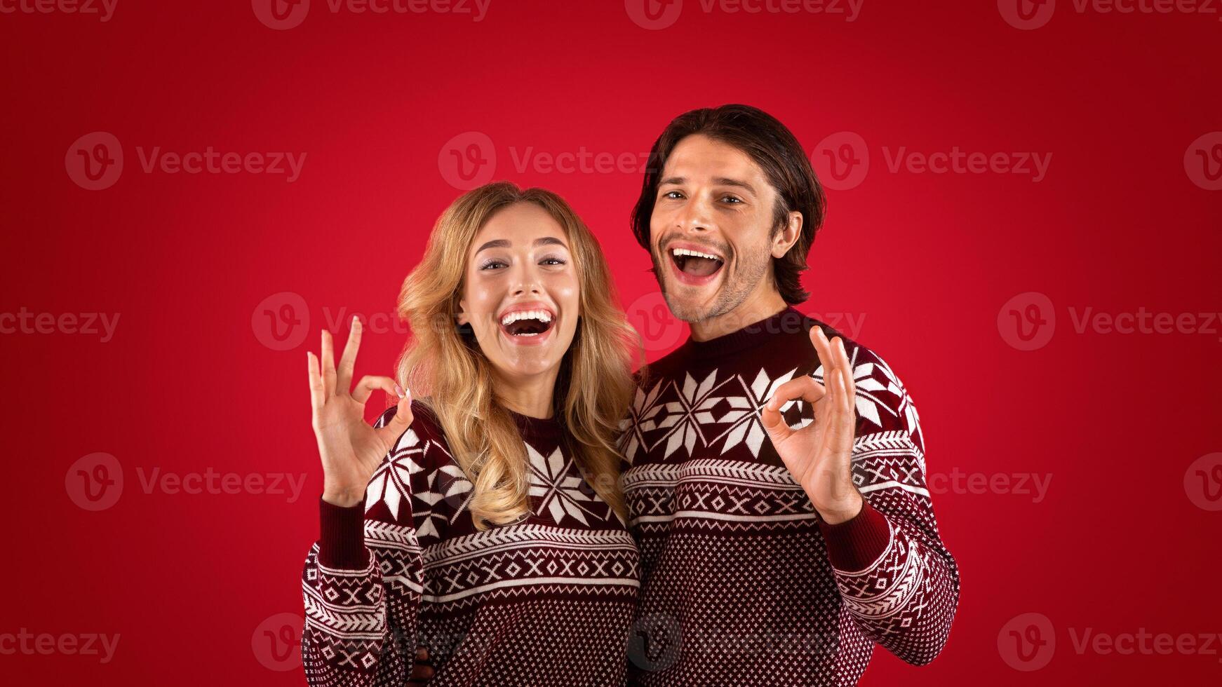 Xmas time. Excited girl with her boyfriend showing OK gestures on red background, panorama photo