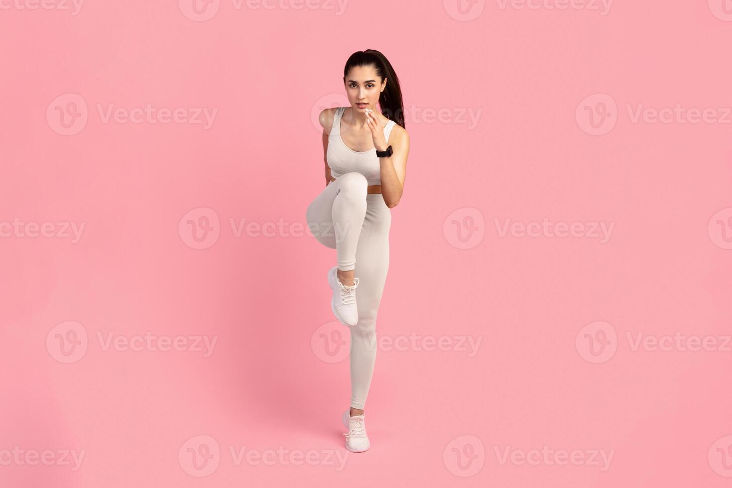 Running Competition. Full length front vertical portrait of confident young woman in sportswear running and looking towards camera, isolated over pink studio background. Lady jogging and sprinting photo