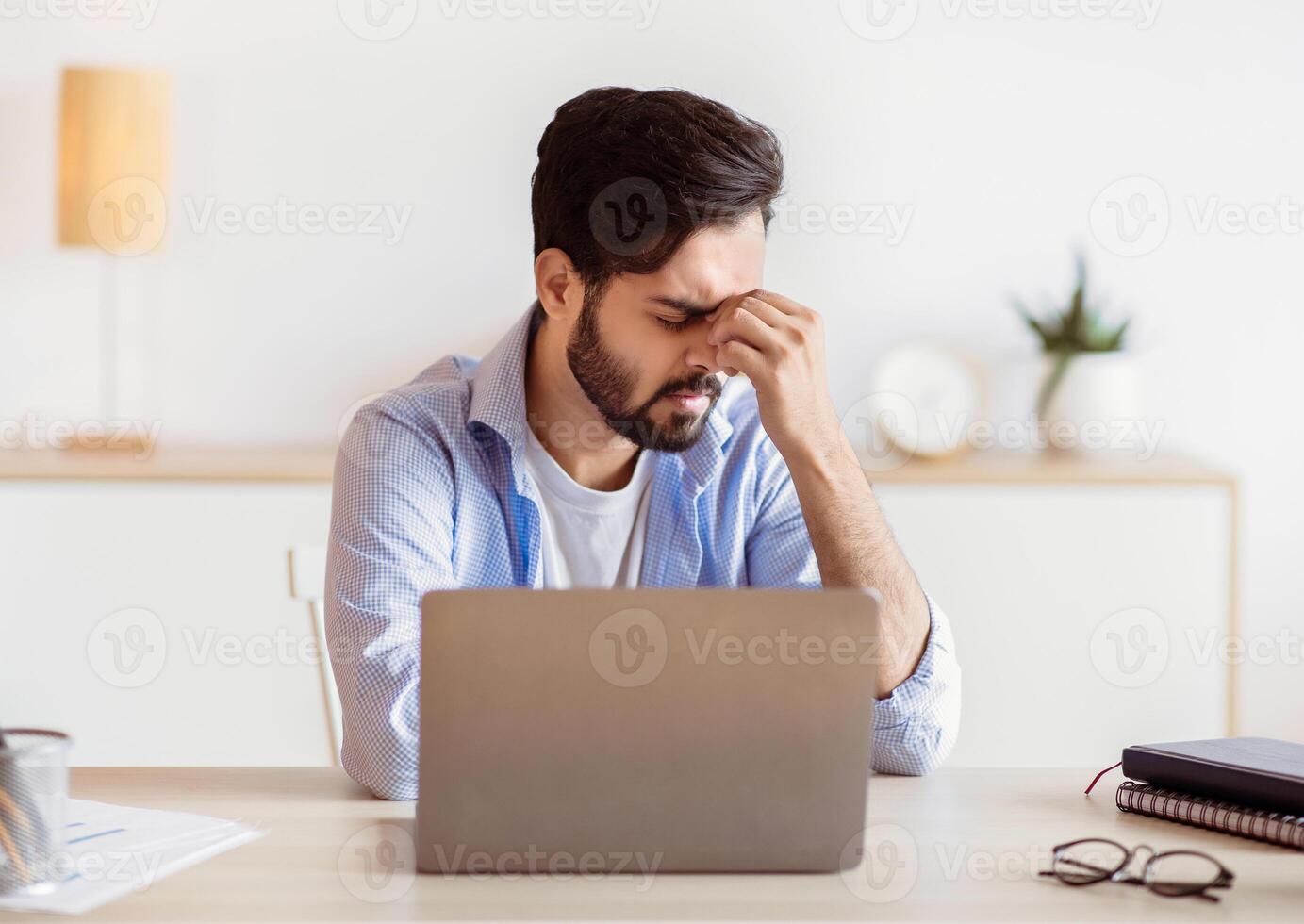 Desperate Eastern Freelancer Guy Sitting At Desk With Laptop, Suffering Lack Of Inspiration Or Feeling Headache, Stressed Young Arab Businessman Having Problems At Work, Free Space photo