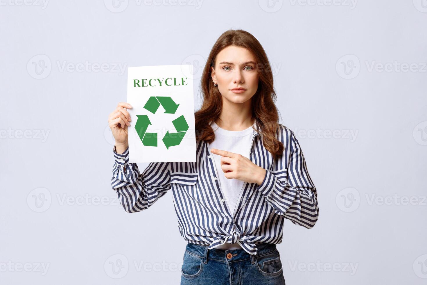 A woman holds a recycling sign, emphasizing the importance of eco-friendly habits. She is dressed casually and engages viewers in a sustainable conversation, likely in an indoor environment. photo