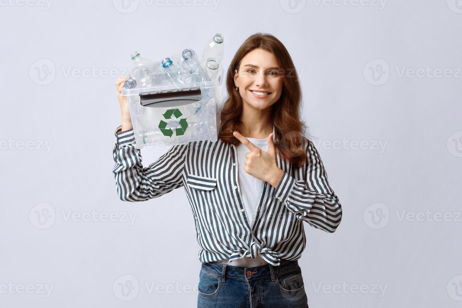 Cheerful Volunteer Woman Pointing At Container With Plastic Waste For Recycling In Her Hands, Smiling Millennial Lady Promoting Garbage Sorting And Eco-Friendly Living, Standing On Gray Background photo