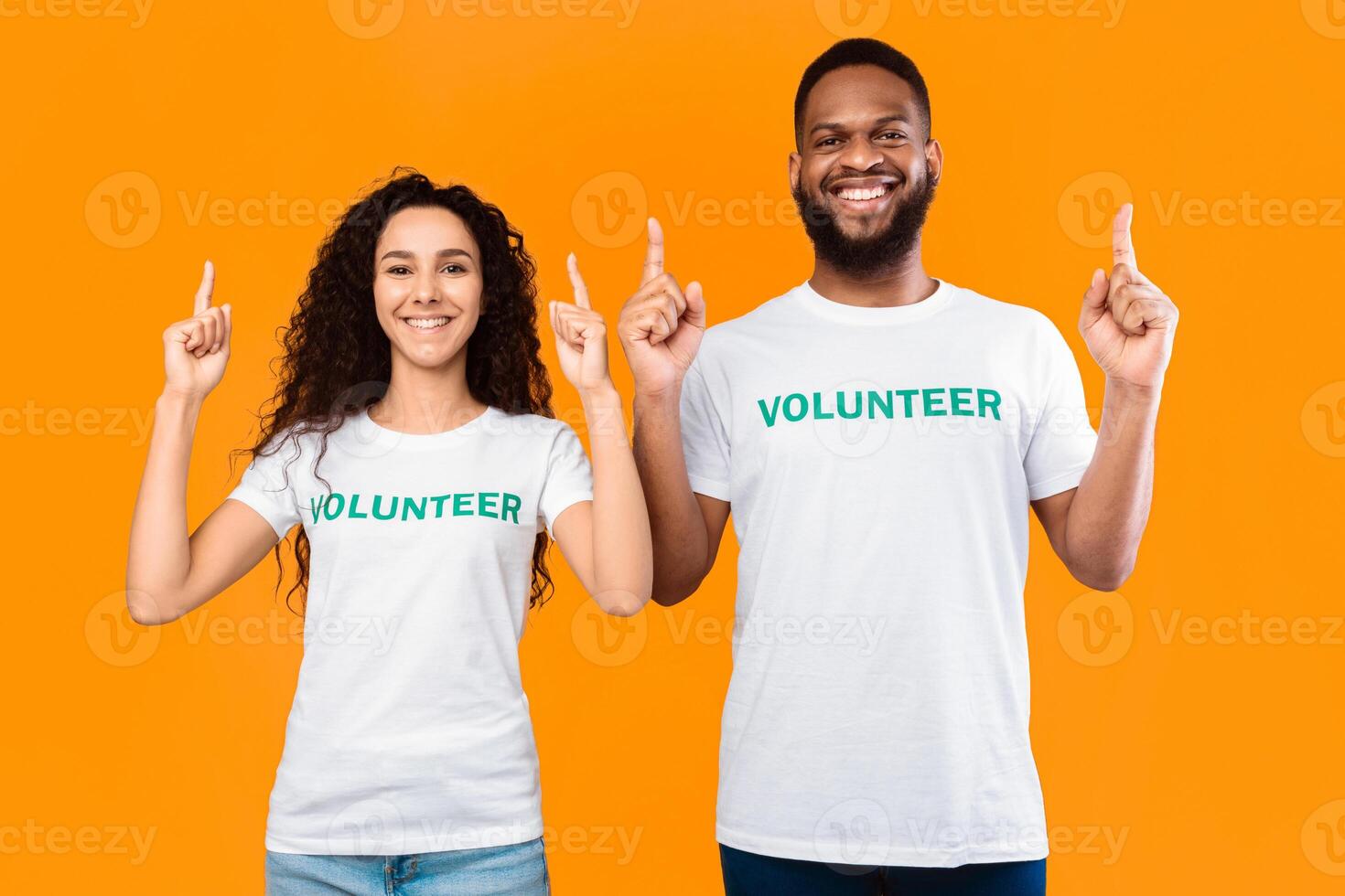 Look There. Female And Male Volunteers Couple Pointing Fingers Up Advertising And Recommending Something Posing Over Yellow Studio Background. Volunteering And Charity Advertisement Concept photo