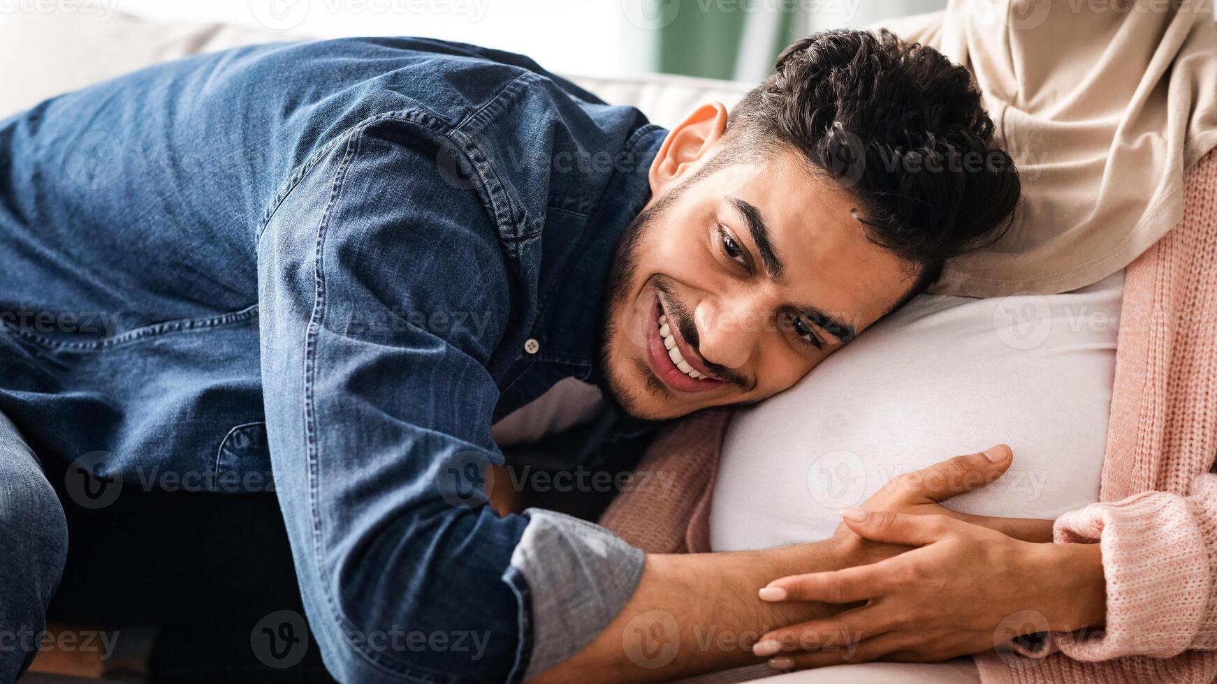 Happy Father. Joyful middle eastern man listening his pregnant wife's tummy, young arab guy tenderly hugging belly of expectant spouse, trying to feel baby kicks, cropped image, closeup photo