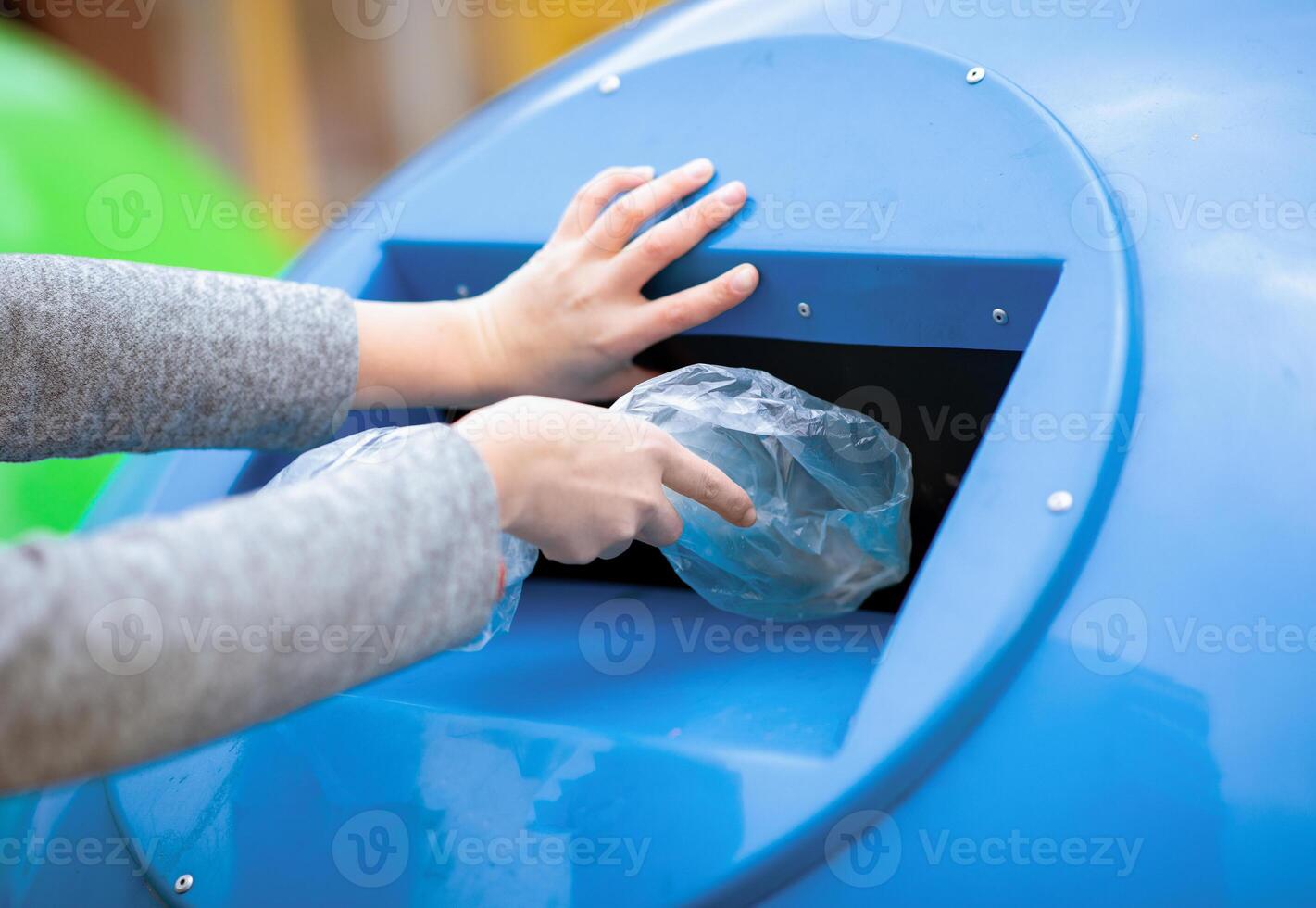Waste Sorting Concept. Hand throwing single use plastic bag into blue recycle bin outdoors, unrecognizable lady caring about environment pollution level, cropped image, closeup photo