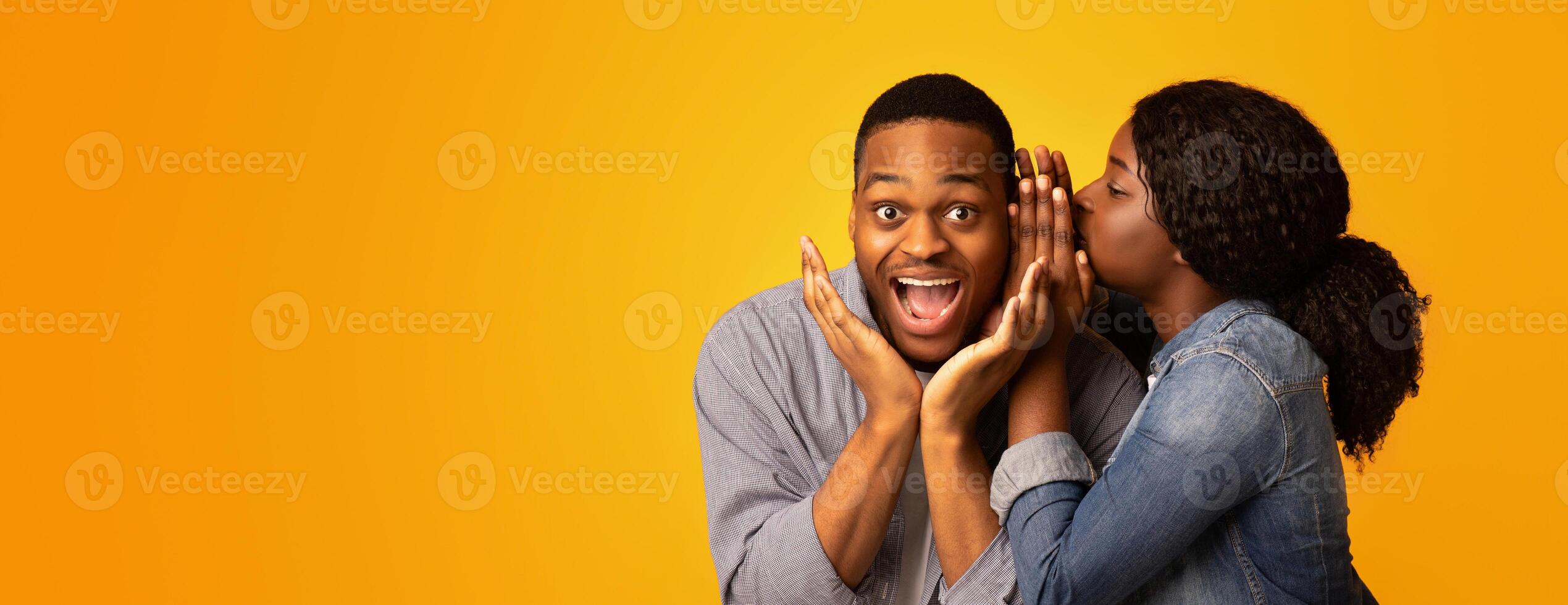 Gossips Concept. Black Woman Sharing Secret With Her Excited Boyfriend, Surprised African American Guy Opening Mouth In Amazement While Standing Together Over Yellow Studio Background, Free Space photo
