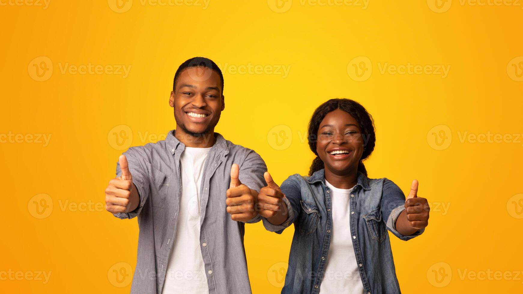 We Recommend. Portrait of cheerful african american couple gesturing thumbs up at camera, expressing approval, joyful black man and woman standing isolated on yellow background, copy space photo