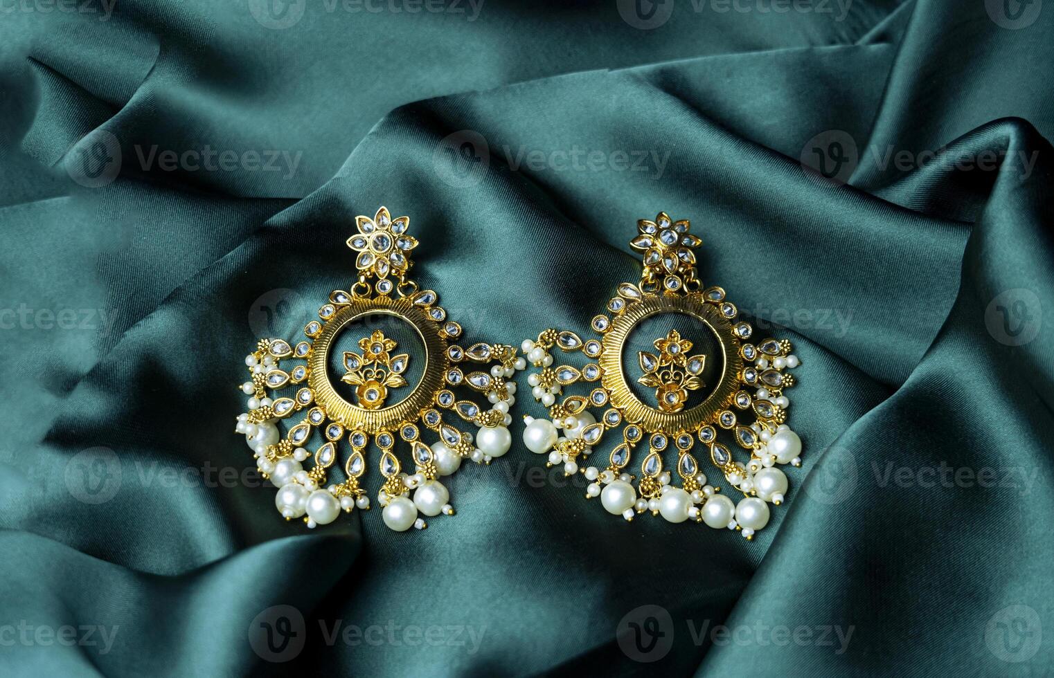 Stylish gold pearl earrings beautifully laid on green fabric photo