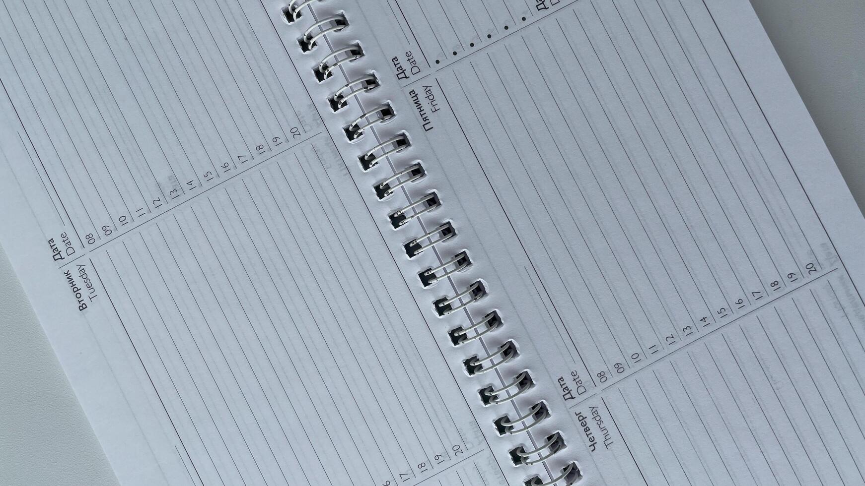 Minimalist close-up of an open spiral-bound weekly planner featuring days of the week in both Russian and English. Perfect for illustrating organization, productivity, and time management in international or bilingual settings. Ideal for business, educati photo