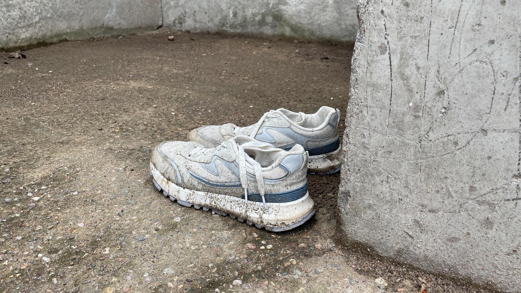 A pair of dirty white sneakers leaning against a wall photo