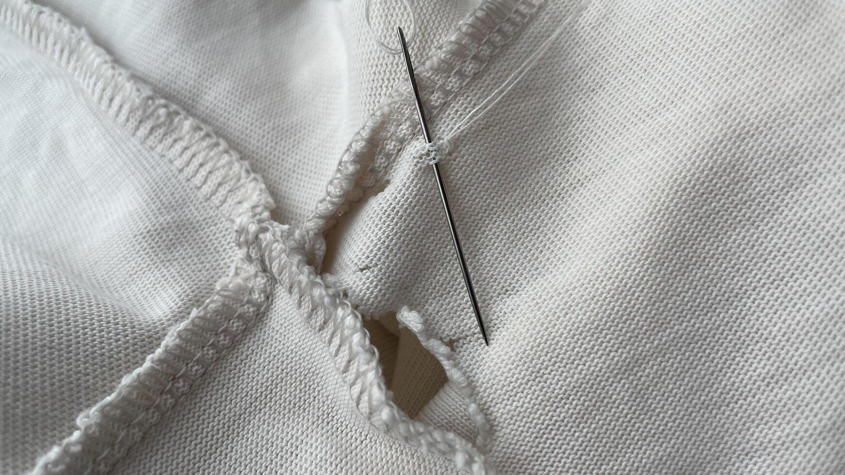 needle and thread sewing holes in beige waxed fabric, close-up, seams and texture, torn old clothes photo