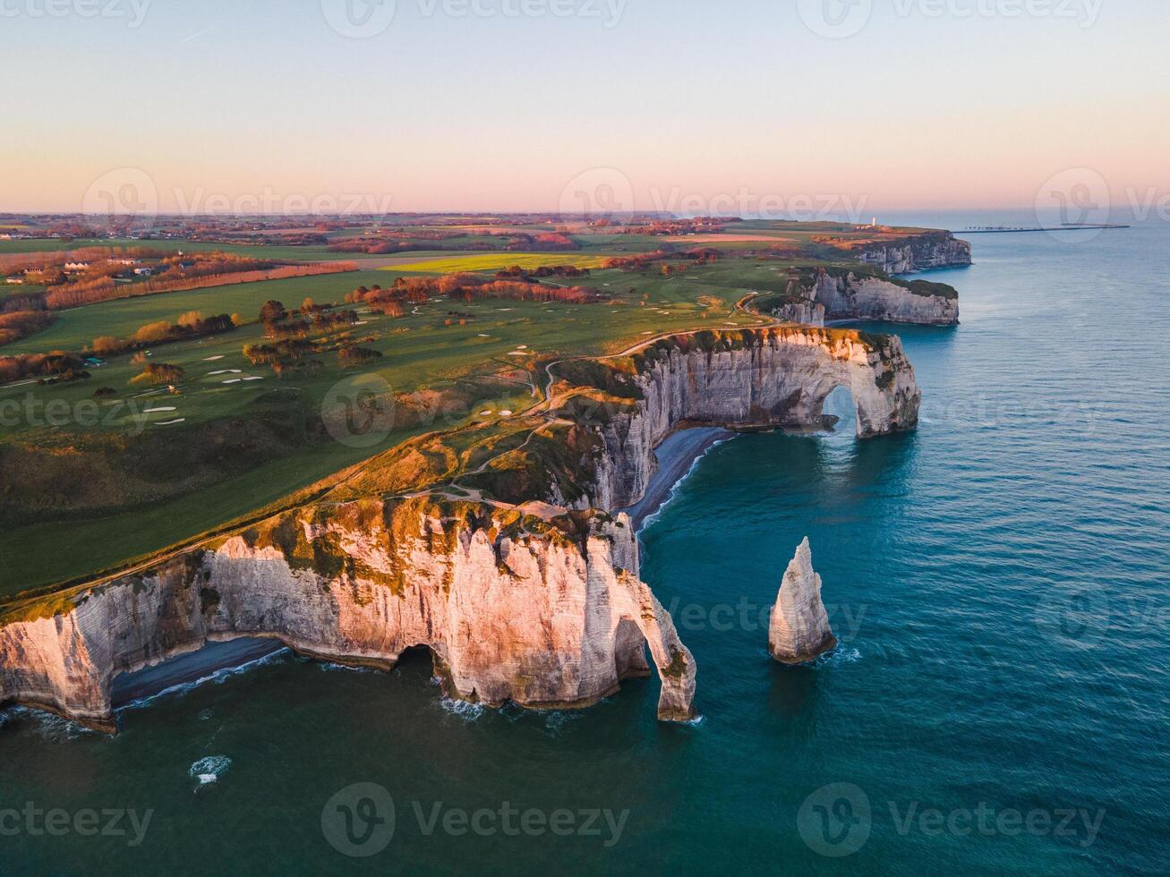 Iconic chalk cliffs and turquoise waters of Etretat glow under sunlight, showcasing Normandy's natural beauty and peaceful coastline. photo