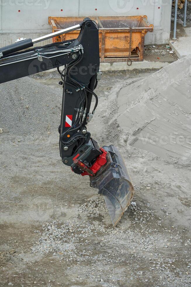 Excavator bucket in action, scooping soil at a construction site. The black boom highlights the machine's industrial design. photo