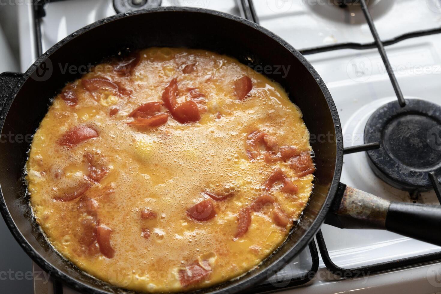 scrambled eggs with tomatoes in a frying pan on a gas stove photo