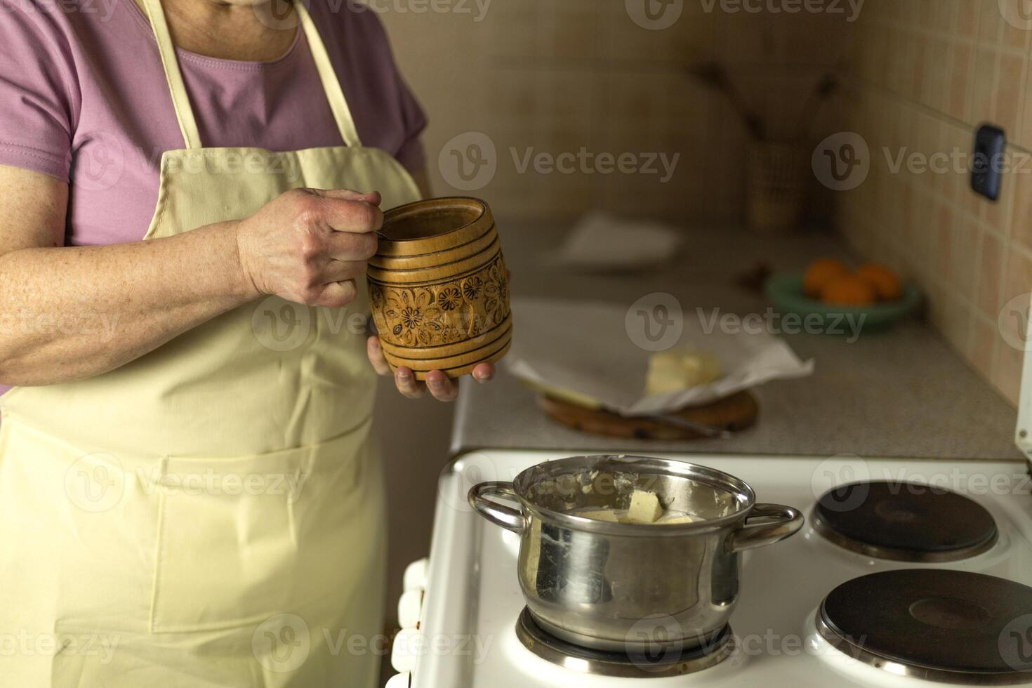 The hands of a senior woman add salt to sweet butter on the stove photo