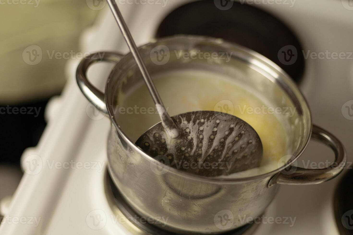stirring sweet cream ghee in a saucepan with a metal spoon with holes photo