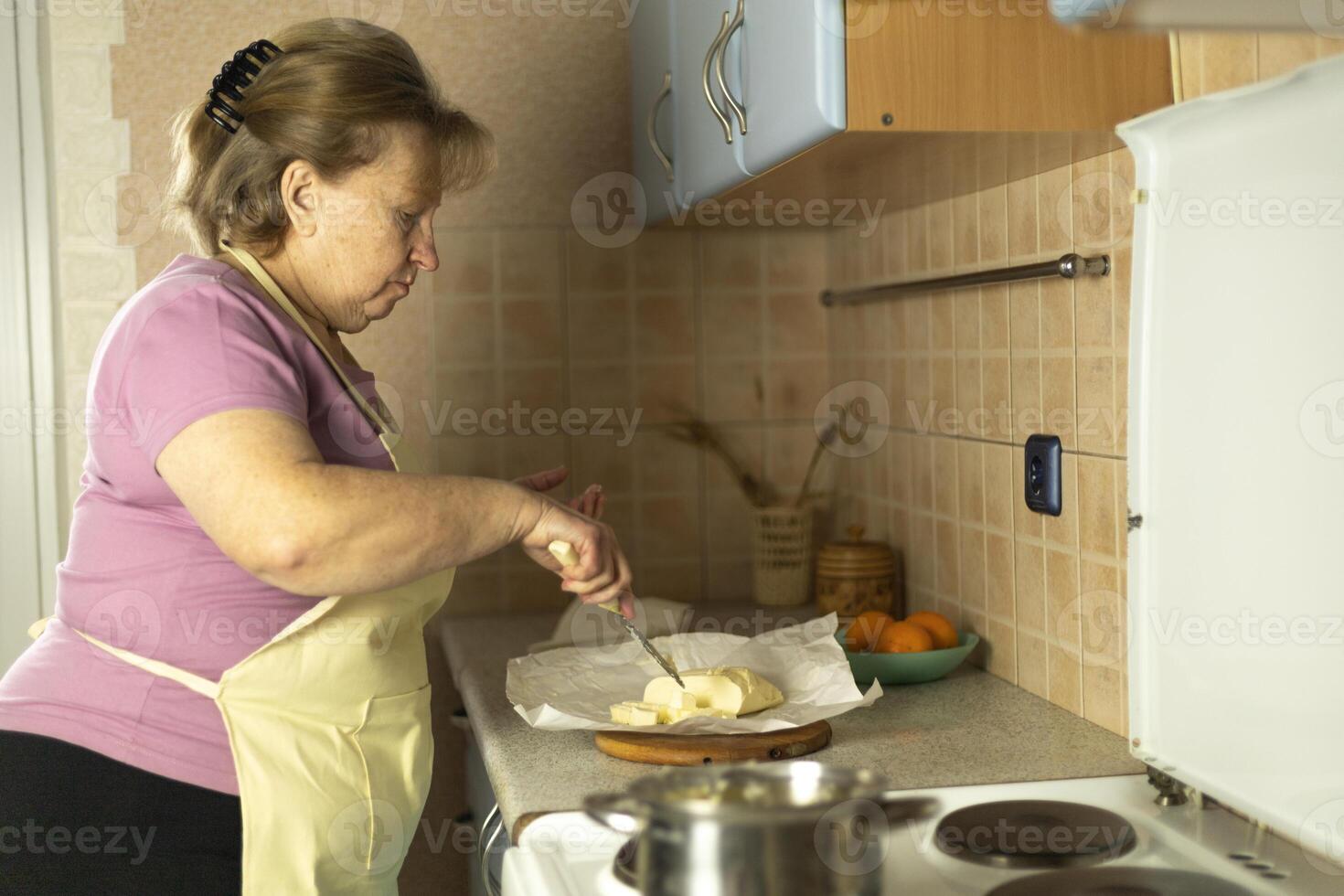 Senior woman in an apron preparing sweet butter for heating on an electric stove, preparing ghee butter photo