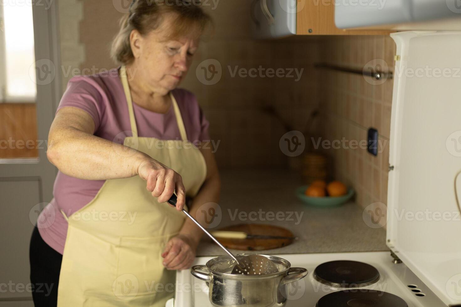 Senior woman stirring melted butter in a saucepan on the stove photo