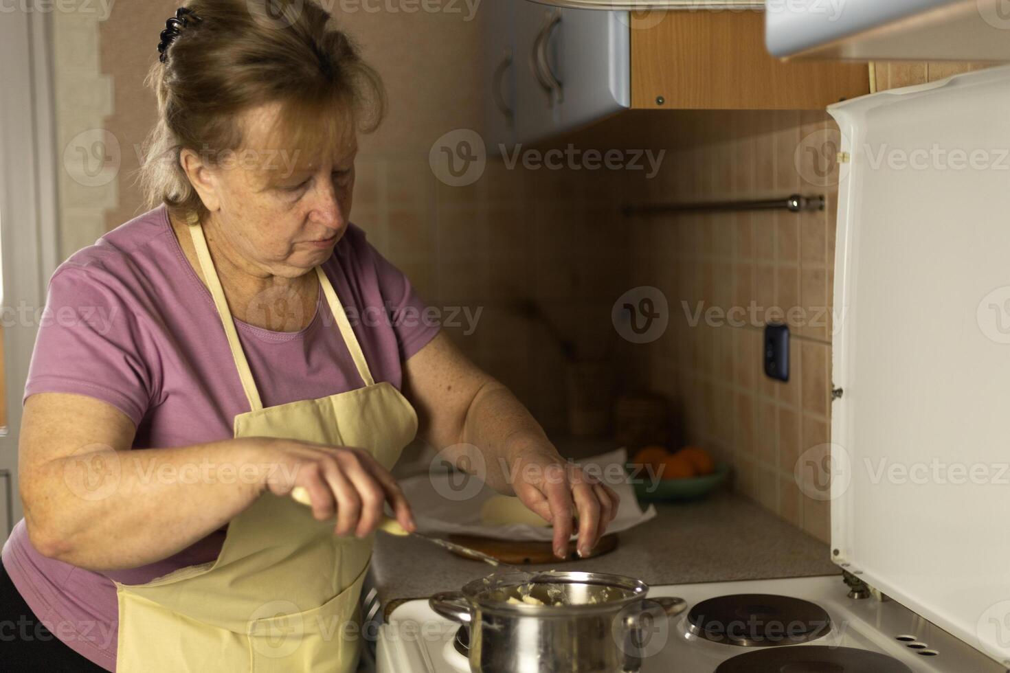 Senior woman in an apron preparing sweet butter for heating on a stove, preparing ghee butter photo