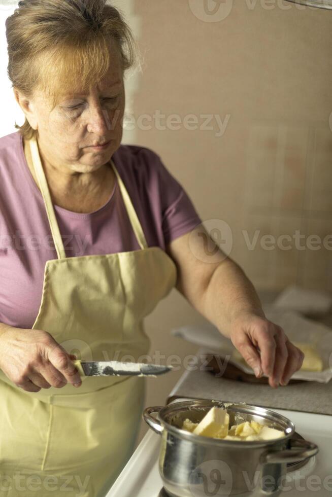 A senior woman puts pieces of sweet butter into a saucepan. photo