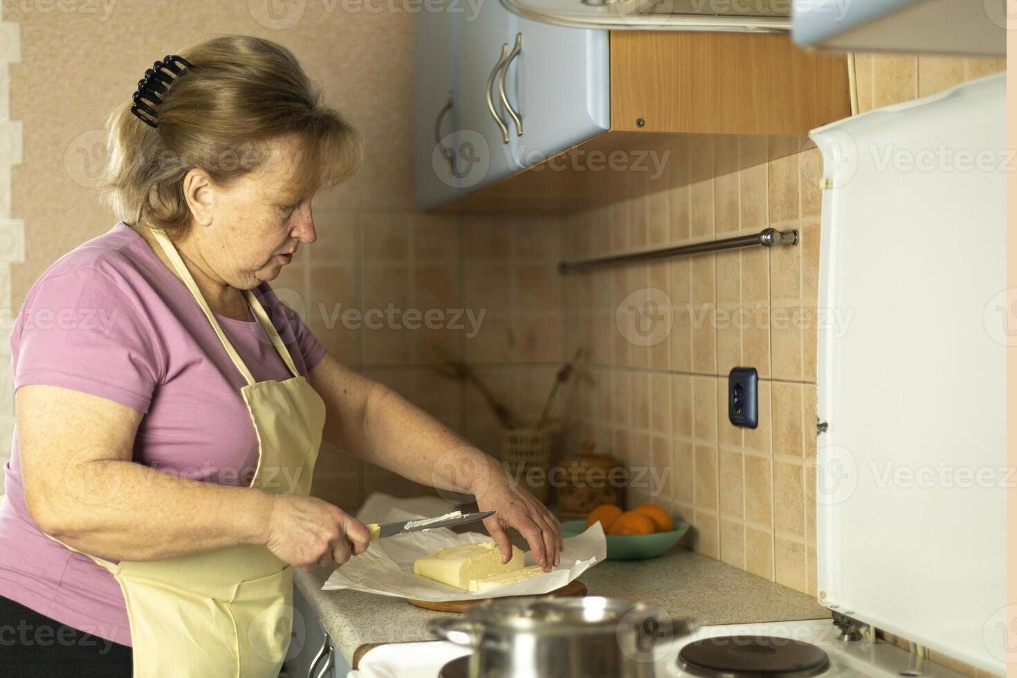 Senior woman in an apron preparing sweet butter for heating, making ghee photo