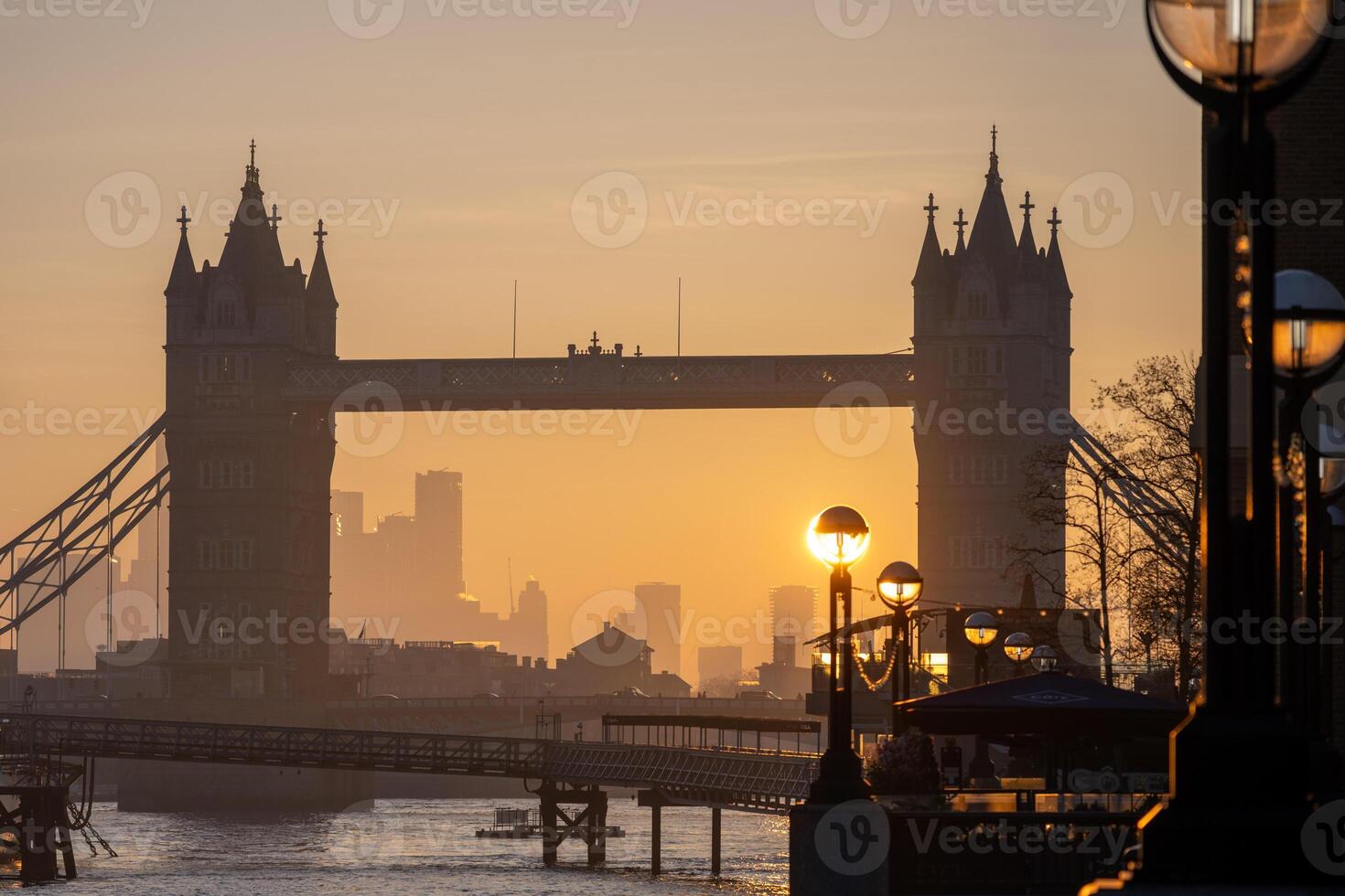 Sunrise casts a warm glow on Tower Bridge as it stands majestically over the River Thames. The surrounding city skyline fades into the background, creating a stunning silhouette. photo