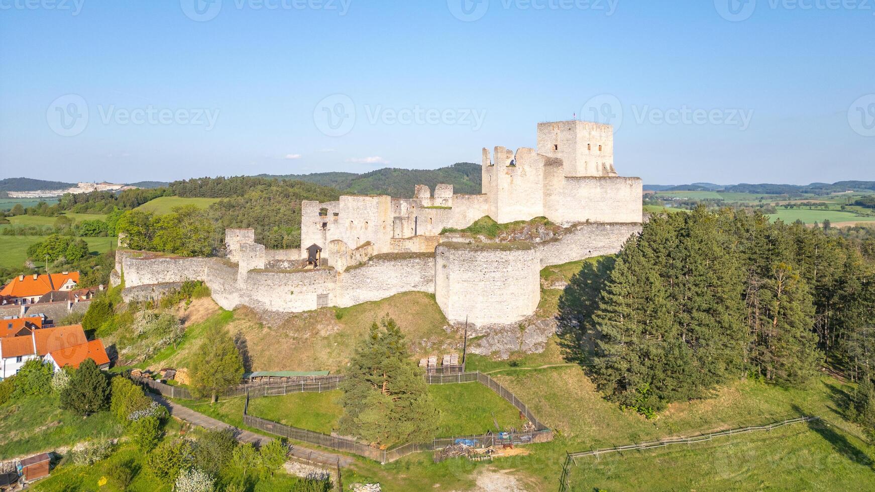 Rabi Castle ruins stand majestically against the backdrop of Czech countryside. This drone view showcases the historical structure surrounded by lush greenery and distant hills on a clear day. photo