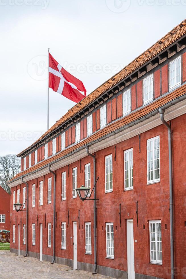 The historic barracks of Kastellet feature striking red buildings and a prominent Danish flag. Visitors appreciate the architecture and rich history while strolling around the site. photo