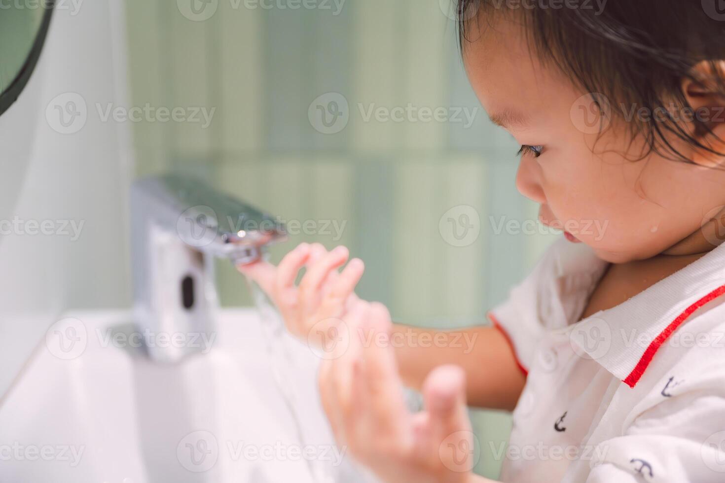 Close-up of Asian boy playing with water from a faucet, Toddler boy curiously turning off the faucet with his hand while water is flowing, Child learning about the world around him, 2 year old son. photo