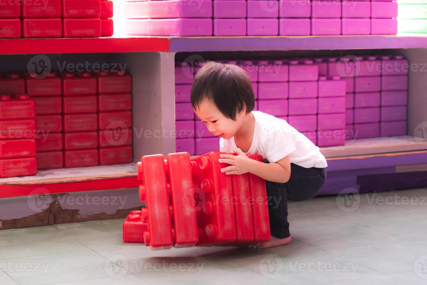 Asian boy playing with big red building blocks, child moving toys, learning through play, development of muscles of different parts of the body. 2 year old son. photo