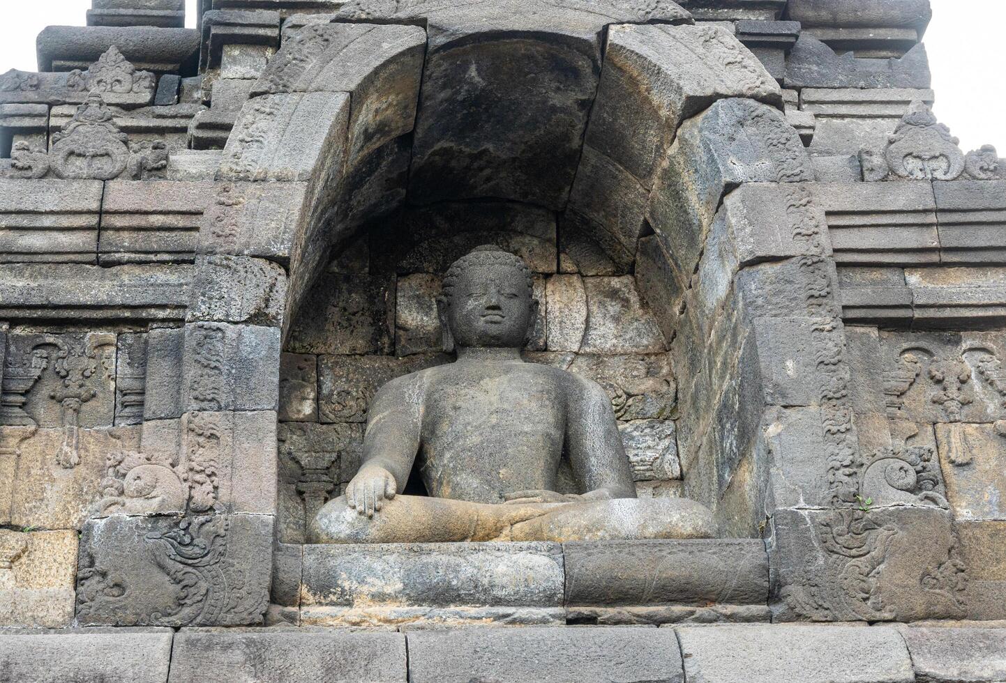 A Buddha statue sits calmly in a stone niche on Borobudur temple, surrounded by ancient carvings. photo