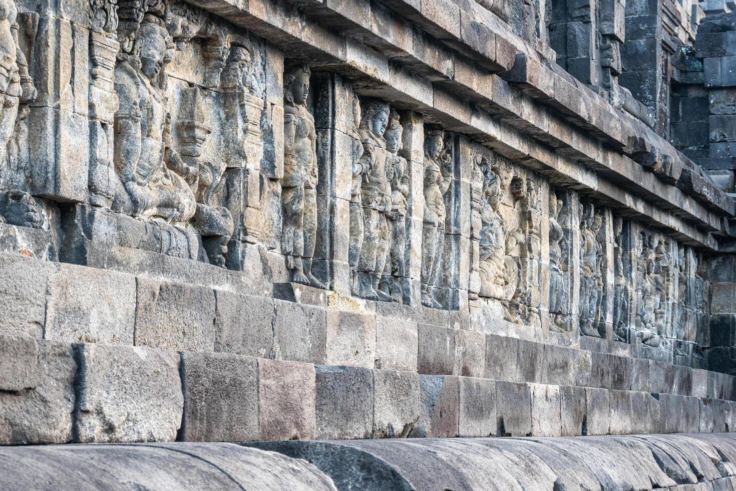 Ancient stone carvings on a temple wall, depicting standing and seated human figures. photo