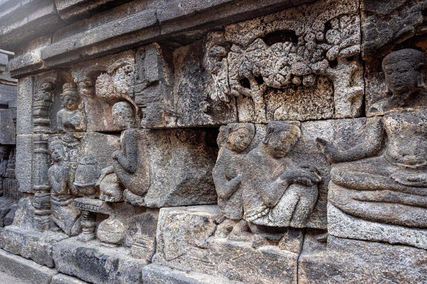 Ancient stone relief showing people, trees, and intricate carvings on a temple wall. photo